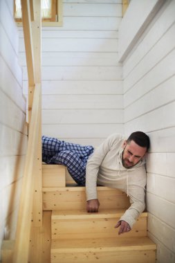 Evde ahşap merdiven üzerinde yatan ve yüksek mesafeden düşen sonra ağrıya sarılarak Homewear genç Kafkas adam