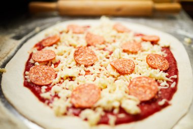 Domates ketçap, rendelenmiş peynir ve salam dilimleri ile çiğ haddelenmiş hamur kavrulmaya hazır