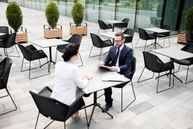From above view of elegant man and woman sitting at table of modern terrace outdoors with clipboard and talking