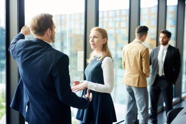Genç ve olgun delegeler ortak sunumu tartışırken konferans salonunun penceresinde duruyorlar.