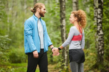 Genç sporcu kadın ormanda spor yaparken eşinin ya da erkek arkadaşının eline dokunuyor.