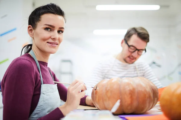 Jovencita Morena Alegre Confiada Delantal Sentada Mesa Pintando Calabaza Estudio — Foto de Stock