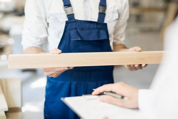 Joven Trabajador Overoles Sosteniendo Tablón Madera Mientras Muestra Colega Taller —  Fotos de Stock