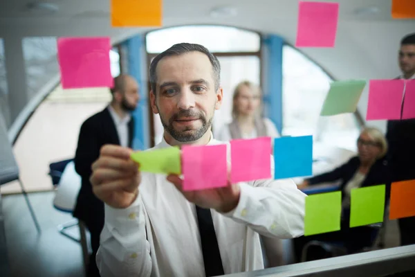 Selbstbewusster Geschäftsmann Klebt Zettel Auf Transparente Tafel Büro Während Die — Stockfoto