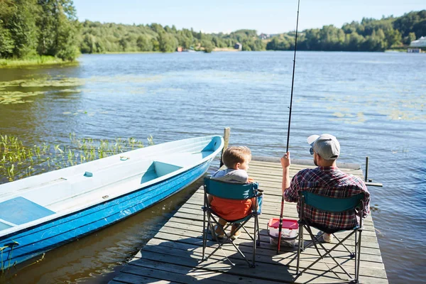 父と息子は桟橋の椅子に座り 美しい自然の中で一緒に釣りをする — ストック写真