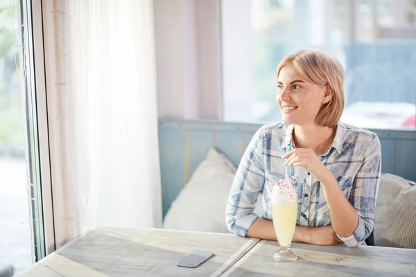 カフェのテーブルのそばに座り 窓を見てミルクカクテルを飲む魅力的な女性 — ストック写真