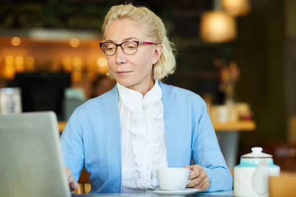 严重的老年金发碧眼的女人在咖啡馆喝茶时在网上寻找东西 — 图库照片