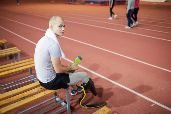 トレーニング後のベンチに休憩と軽食を持つ障害者の右脚を持つアクティブな若者 — ストック写真