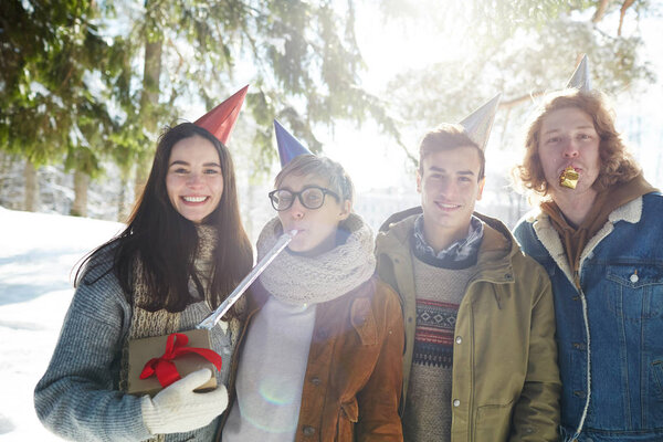 Группа из четырех молодых людей, празднующих Рождество на открытом воздухе в красивом лесу, все в шапках вечеринки
