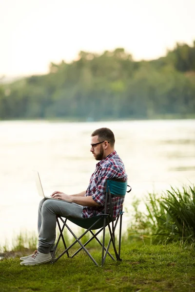 活跃和移动的年轻人与笔记本电脑坐在河边和联网在该国 — 图库照片