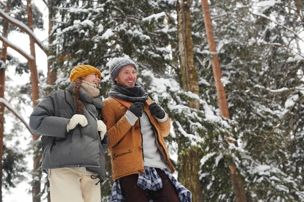 Cheerful excited young friends with backpacks walking in winter forest and discussing route of travel