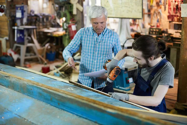Młody Inżynier Wierci Drewnianą Deskę Podczas Gdy Jego Starszy Kolega — Zdjęcie stockowe