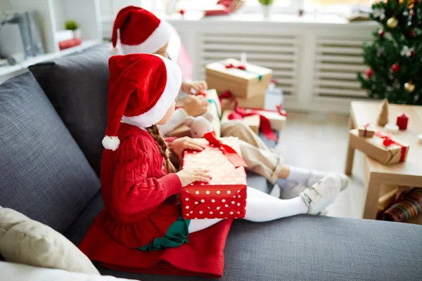 ソファに座って 彼らのクリスマスプレゼントと箱を開梱する2人の小さなサンタの女の子 — ストック写真