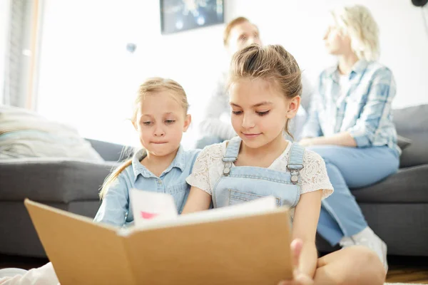 リビングルームの床で休みながらそれを読んで開いた本を持つ小さな未就学児 — ストック写真