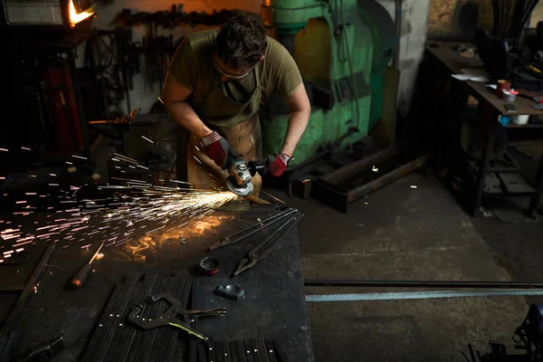 铁匠在工作服使用电动手工具加工铁工件在铁匠 — 图库照片