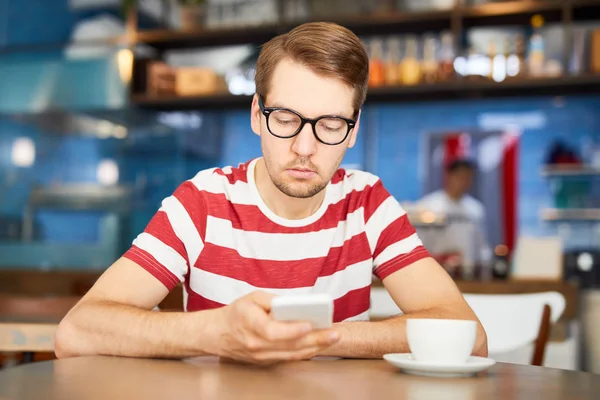 Gözlüklü Çizgili Tişörtlü Genç Adam Kafede Vakit Geçirirken Akıllı Telefonuyla — Stok fotoğraf