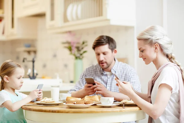 所有家庭在午餐时使用智能手机 集中的年轻家庭沉迷于技术上网 同时在舒适的厨房吃早餐 — 图库照片
