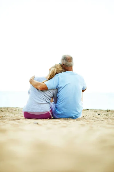 后视图深情的老夫妇坐在沙滩上拥抱和放松后锻炼 — 图库照片