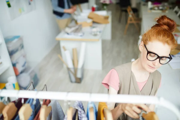 Young Female Designer Fashion Standing Rack While Choosing Casual Clothes — 스톡 사진