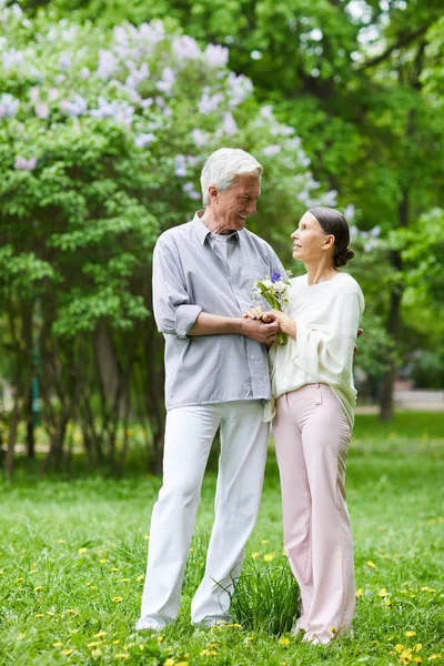 Seniorzy Casualwear Patrząc Siebie Stojąc Zielonym Trawniku Kwitnącym Parku — Zdjęcie stockowe