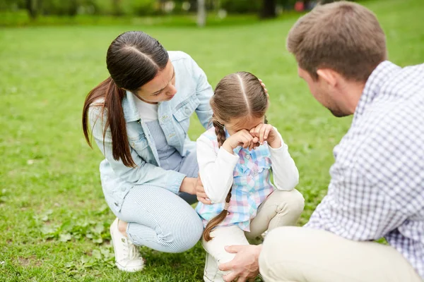 草の上に座っている間に泣いている小さな女の子と彼女の両親は週末の寒さの間に彼女を慰める — ストック写真