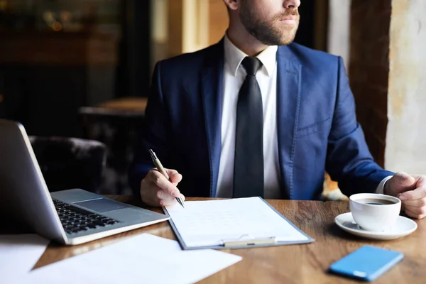 テーブルに座って レストラン コーヒーカップ ラップトップ テーブルの上の紙で働いている間 スーツを着た深刻なひげのビジネスマンのクローズアップ — ストック写真