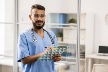 Karışık ırk adam gözlük ve mavi üniforma tıbbi notları belge içinde yapım genç sakallı