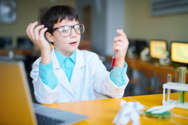 Whitecoat 'ta elinde kırmızı sıvıyla içki şişesi tutan genç bir öğrenci çeşitli kimyasal maddeler üzerinde çalışıyor.