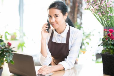 Genç esmer kadın işyeri tarafından istemciler telefon ve online danışmanlık yaparken bakıyorsun önlük