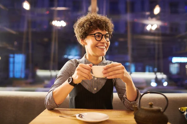 豪華なカフェのテーブルに座っているスマート カジュアルでお茶を飲んで 素敵な夜を楽しんで 若い陽気な女性 — ストック写真