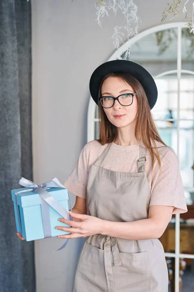 Långhåriga Kvinna Förkläde Hatt Och Glasögon Håller Blå Giftbox Bunden — Stockfoto