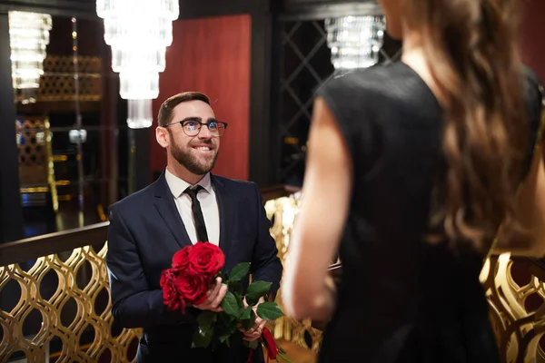 彼のガール フレンドの彼女を見ながら赤いバラの花束を持ってエレガントなスーツで幸せな若い男 — ストック写真