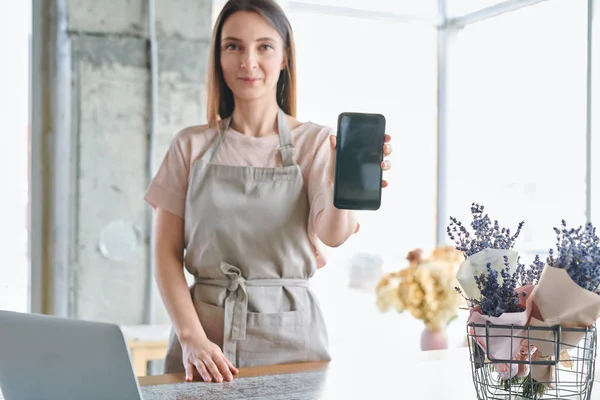 花の店の広告をスマート フォン画面上に示す作業服の若い自信を持って女性 — ストック写真