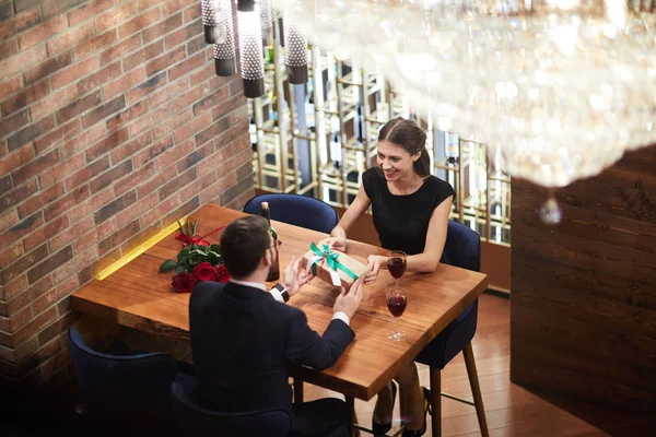 ギフト ボックスを取って幸せな若い女は上品なレストランでロマンチックな日付の間にテーブルによって彼女の彼氏に渡す — ストック写真