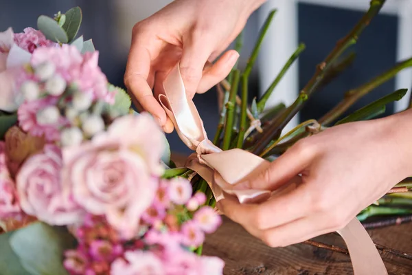若い女性の手の結び目を結ぶことと花の束の周りベージュのシルクのリボンを固定しながら弓を作る — ストック写真