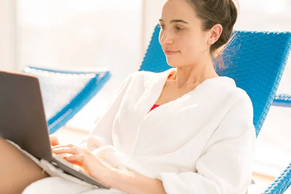 バスローブ夏のリゾート地でデッキチェアの上 ノート パソコンの前にネットのブラウジングの若い女性 — ストック写真