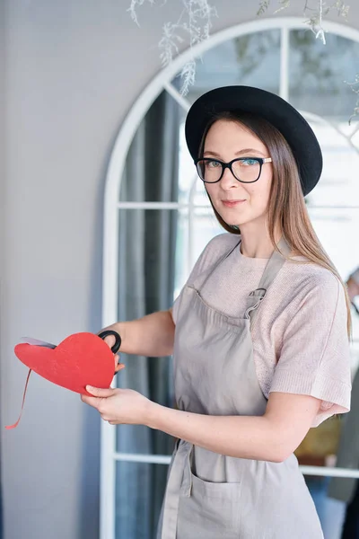 エプロンやスタジオでカメラの前に立って帽子切削赤い紙のハートでかわいい女の子 — ストック写真