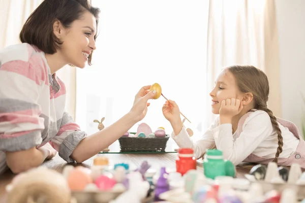 小女孩和她的母亲用金色的油漆或水粉覆盖着一个复活节彩蛋 — 图库照片