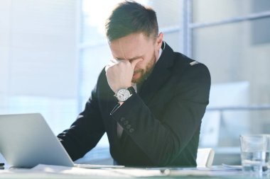 Ofiste dizüstü bilgisayar önünde otururken konsantre olmaya çalışan formalgiyim gergin ve yorgun genç işadamı