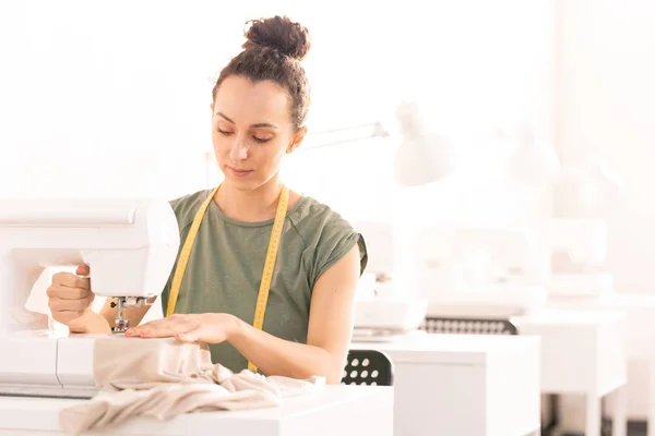 若いブルネットのお針子は ファッションコレクションのための新しい服を縫製しながら ワークショップで機械で座って — ストック写真