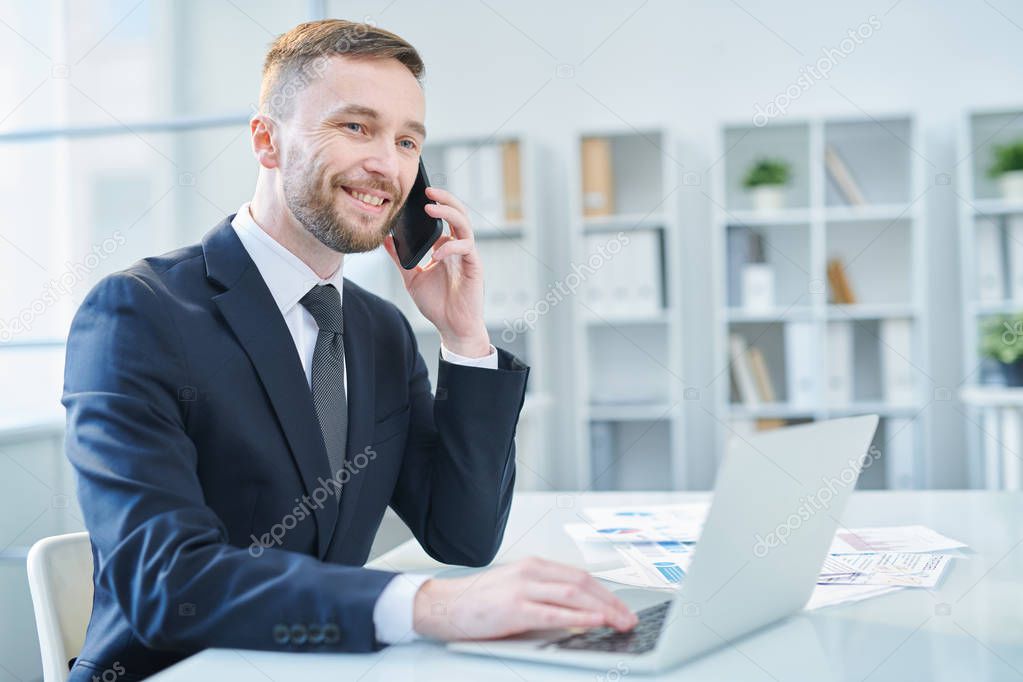 Successful elegant businessman in suit consulting client on smartphone while browsing in the net