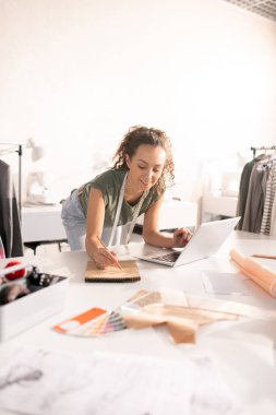 Çalışma alanı tarafından yeni moda koleksiyonu üzerinde çalışırken not defteri 'nde kroki yapan genç yaratıcı kadın