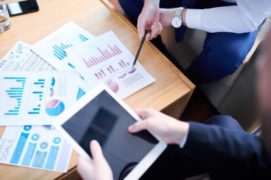 Kalemi olan ve masadaki finansal verilerle kağıda işaret eden ve dokunmatik yüzeyli çalışana açıklayan işadamı