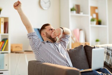 Bir Kol germe sırasında dizüstü bilgisayar ve esneme önünde kanepede oturan giyim genç yorgun Freelancer