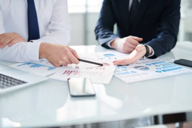 Formalite giyen iki genç işadamı finansal belgeleri tartışırken, biri diyagramı işaret ediyor