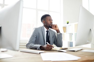 Bilgisayar ekranında verilere bakarak Genç dalgın işadamı çalışma alanına göre defter notları yaparken