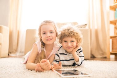 Sevimli mutlu kız ve tablet ile onu sevimli kardeşi boş oturma odası katında yatıyor