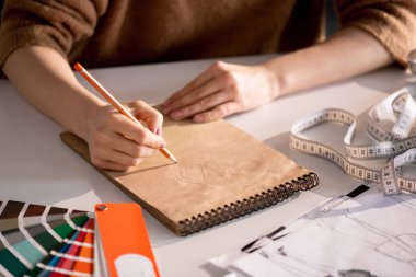 Atölye masasında otururken not defterinde yaratıcı moda tasarımcısı çizim eller