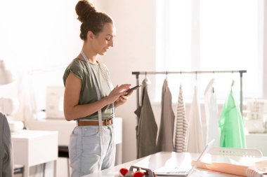 Tasarım stüdyosunda çalışma sırasında akıllı telefonda neşeli kendini istihdam moda tasarımcısı kaydırma