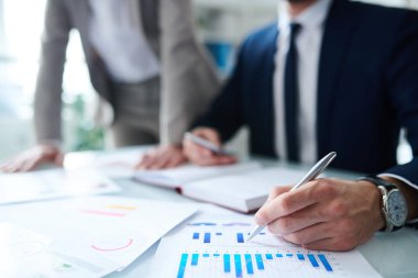 Mali belgede mavi grafiği işaret eden kalemli işadamı, bunu iş arkadaşına gösterirken ve açıklarken